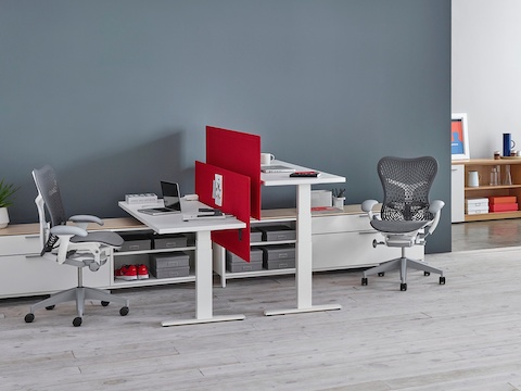 Red privacy screens separate two white Motia Sit-to-Stand Tables facing each other at seated and standing heights. Red privacy screens separate two white Motia Sit-to-Stand Tables facing each other at seated and standing heights.