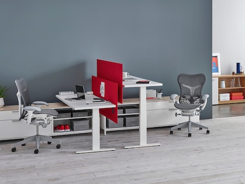 Red privacy screens separate two white Motia Sit-to-Stand Tables facing each other at seated and standing heights.