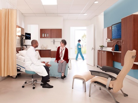 A doctor and patient converse in a patient room equipped with a Nala Patient Chair and ottoman.