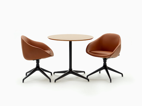 Uma mesa de café Ali com base preta em estrela de 4 pontas e tampo redondo em madeira de carvalho, ao lado de duas cadeiras Always marrons.