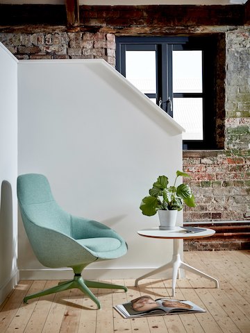Una silla lounge Always tapizada en color verde, equipada con una base giratoria combinada en forma de estrella de 4 puntas, junto a una mesa Ali blanca, ambas de NaughtOne.