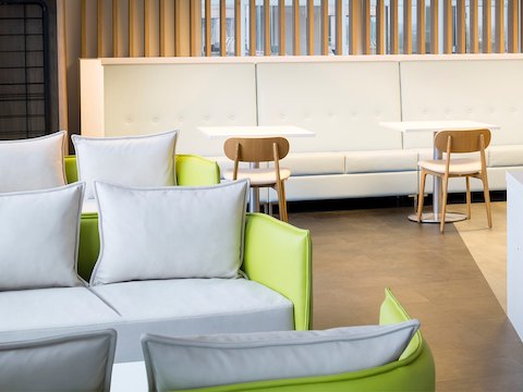Un grupo de sofás simples Cloud de naughtone en gris y verde, en un esquema para usos diversos donde puede verse una cabina larga y mesas de Café con sillas en el fondo.