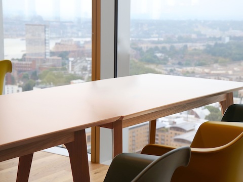 Een beige NaughtOne Dalby-vergadertafel in een hoge conferentieruimte, Eames gegoten plastic stoelen van Herman Miller op de voorgrond.