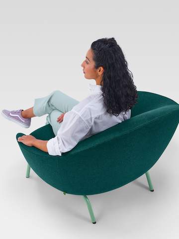 Uma fotografia em ângulo traseiro de uma mulher sentada em uma Lounge Chair Ever verde-escura.