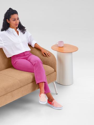 A woman sitting on a camel-coloured two-seat Ever Sofa next to a Tun Side Table.