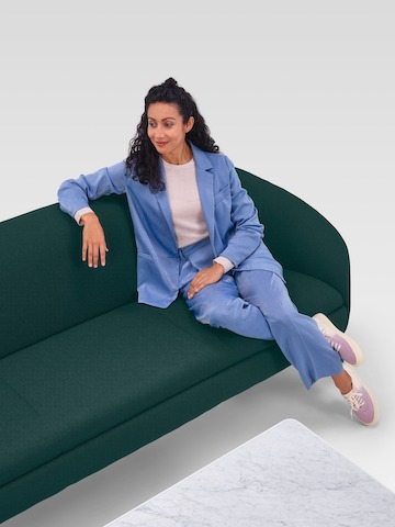 Femme confortablement installée dans un canapé trois places Ever vert foncé, à côté d'une table basse en marbre.