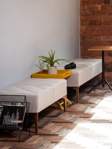 Two light gray Hatch Benches placed along a wall with a Knot Side Table with oak top and black base.