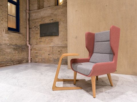 Un sillón Hush de NaughtOne con respaldo rosado y almohadilla del asiento gris claro, con base de madera, visto desde el frente.
