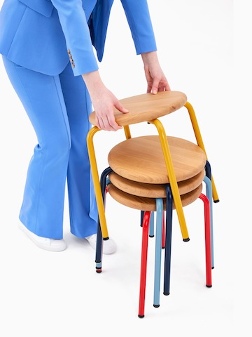 A woman lifting a Penny Stool from a stack.