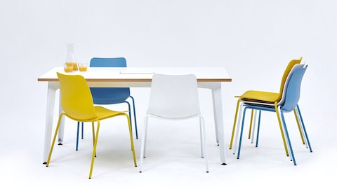 Três cadeiras para visitantes Polly em amarelo, azul e branco em volta de uma mesa de reuniões Fold. Mais três cadeiras Polly empilhadas ao lado da mesa.