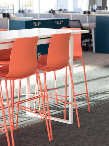 特写镜头：办公环境内，几张摆放在白色吧台桌前的橙色Polly凳子。