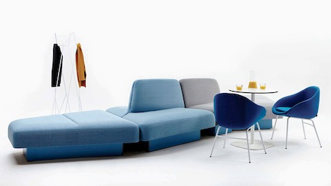 Vista con fondo blanco de un sofá modular amplio con sillas, una mesa y un perchero.