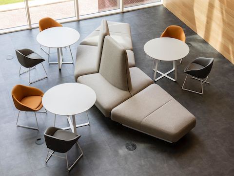 An overhead view of a beige NaughtOne Rhyme Modular Seating arrangement paired with three white Frog Café tables and grey and orange Always Chairs.