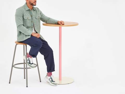 Un uomo è seduto su uno sgabello Penny accanto a un tavolo Tier altezza bar.