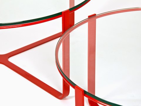 Een close-up van twee rode, ronde Trace-salontafels met glazen blad.