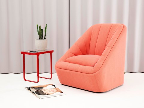A red NaughtOne Trace Side Table with glass top alongside a coral Fiji Chair with a curtain backdrop.
