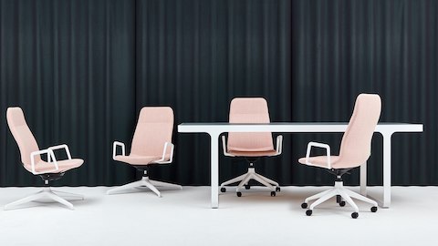 Quattro sedute lounge con braccioli, rivestite in tessuto rosa pallido con basi bianche a 4 e 5 stelle intorno a un tavolo riunione.