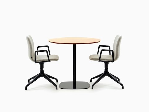 A round oak-topped Ped Café Table with black base between two grey Viv Side Chairs with black armrests and bases.