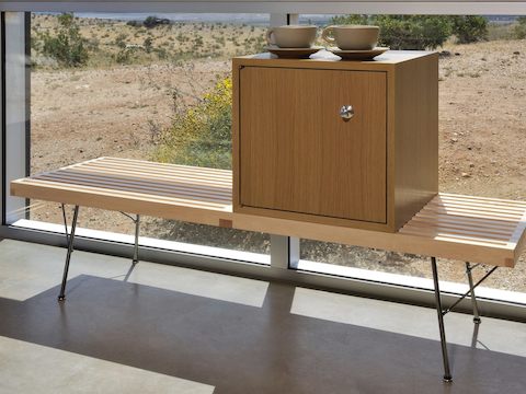 A closed storage module from the Nelson Basic Cabinet Series sits atop a Nelson Platform Bench that abuts a glass wall. 