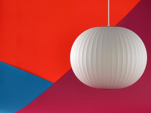 Een Nelson Ball Bubble Pendant-lamp die voor een oranje, rode, en blauwe achtergrond hangt.