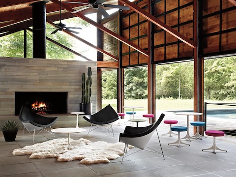 Three black leather Nelson Coconut Lounge Chairs and several Nelson Pedestal Stools in a glass-walled room with a fireplace. 