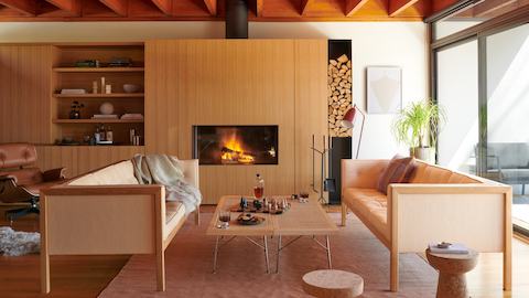 A living space featuring the Nelson Cube Sofa, Nelson Cane Bench, and Eames Lounge Chair accessorised with cork stools, a floor lamp, linen rug, chess set and fireplace tools.