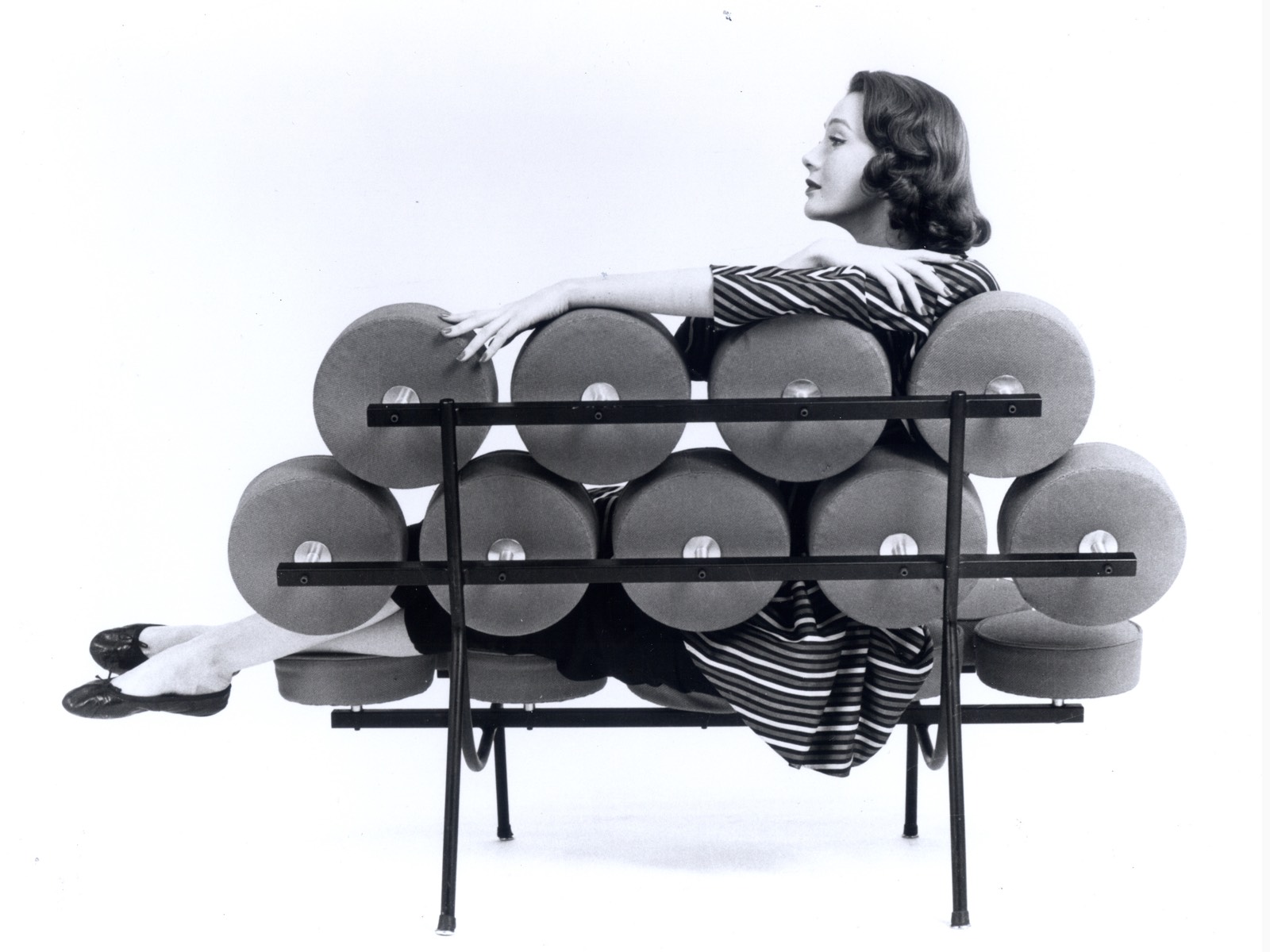 A vintage black-and-white photo of a woman with her feet up on a Nelson Marshmallow Sofa, viewed from behind.