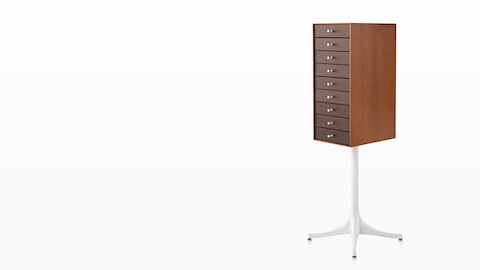 Angled view of a vertical nine-drawer Nelson Miniature Chest with a medium finish and white pedestal base. 