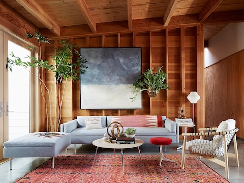 Una sala de estar residencial con un sofá Bolster gris claro y un taburete Nelson Pedestal con un asiento tapizado de color rojo.