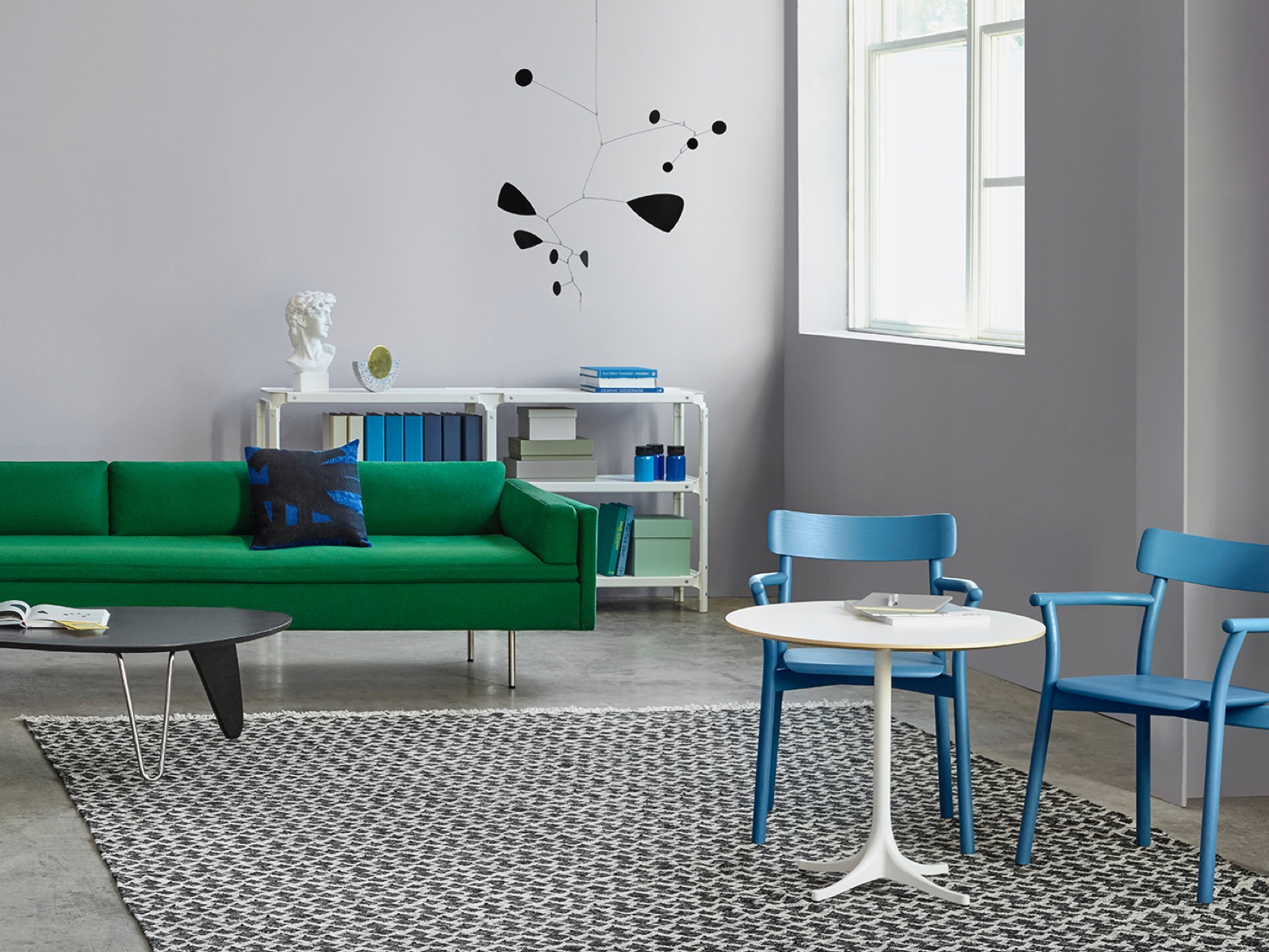 A white Nelson Pedestal Table accents a contemporary space featuring a green Bolster sofa. 