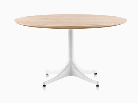 Una mesa de pedestal Nelson redonda con una parte superior de madera clara y base blanca.