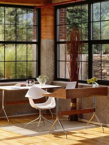 Una oficina en el hogar con una vista exterior, amueblada con un sillón blanco de plástico moldeado Eames y una mesa y escritorio Nelson Swag Leg.
