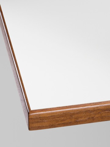 Close-up of the corner detail on a Nelson Swag Leg Table with a white laminate top and walnut veneer edge band.