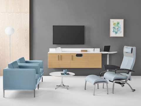 A patient room featuring a Nala Patient Chair in light blue textile with dark grey urethane arm pads, Riva Lounge Chairs in blue textile and a Nelson side table.