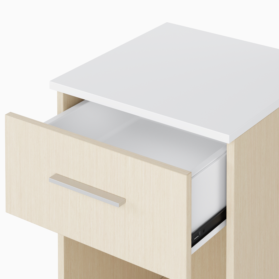 A close-up view of an open drawer with white laminate interior and a white plastic insert on a Nemschoff Bedside Cabinet.