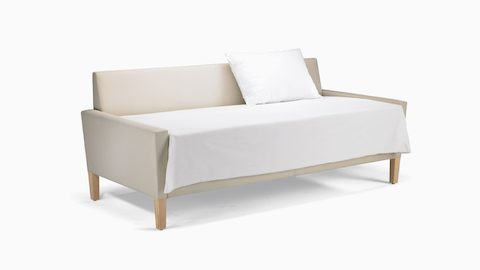 A Brava Flop Sofa in white textile with maple legs converted to sleep surface with sheets and pillow.