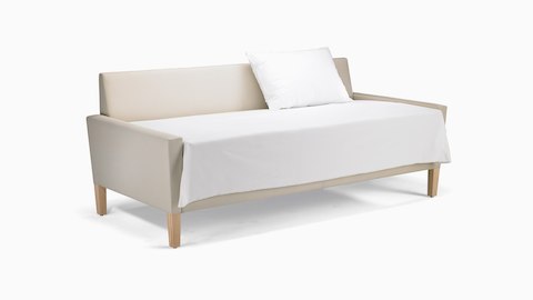 A Brava Flop Sofa in white textile with maple legs converted to sleep surface with sheets and pillow.