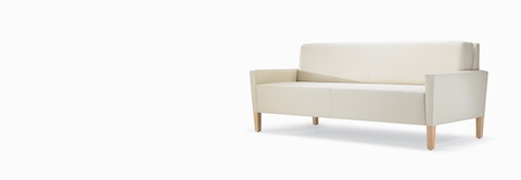 A three-quarter view of a  Brava Flop Sofa in white textile with maple legs.