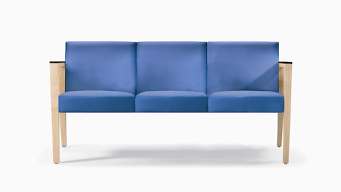 A front view of a Brava 863 Sofa in blue textile with maple base and urethane arm caps.