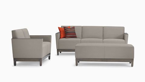 A setting of gray Brava Platform Lounge System products, including a two-seat settee and a three seat sofa with red pillows with wooden arm caps and a bench, all with a wood base.