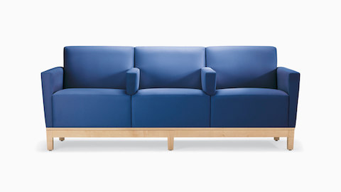 A front view of a Brava Platform Sofa with divider arms in blue textile with maple base.