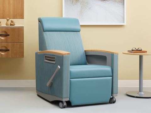 Nemschoff Consoul Recliner in a two-tone blue upholstery and light wood armcaps, set in a patient care space with a small side table next to it.