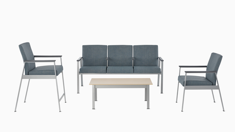 An Easton Easy Access Chair, Easton Multiple Seating with three seats and intervening arms, and an Easton Side Chair, all with blue upholstery, metallic silver frame, and slate gray arm caps across from an Easton Coffee Table with a clear on ash top and metallic silver base. An Easton Easy Access Chair, Easton Multiple Seating with three seats and intervening arms, and an Easton Side Chair, all with blue upholstery, metallic silver frame, and slate gray arm caps across from an Easton Coffee Table with a clear on ash top and metallic silver base.