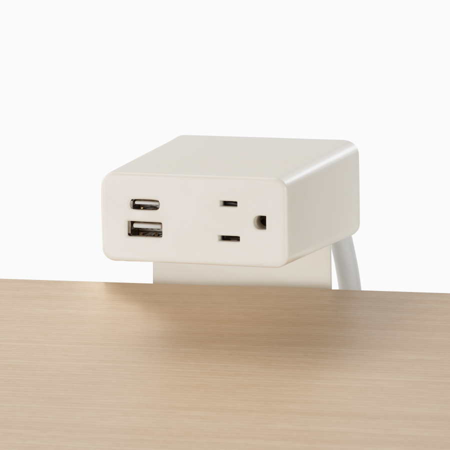 A close-up view of a Logic Mini power unit with two USB ports and one power outlet on top of a clear on ash laminate Easton table.