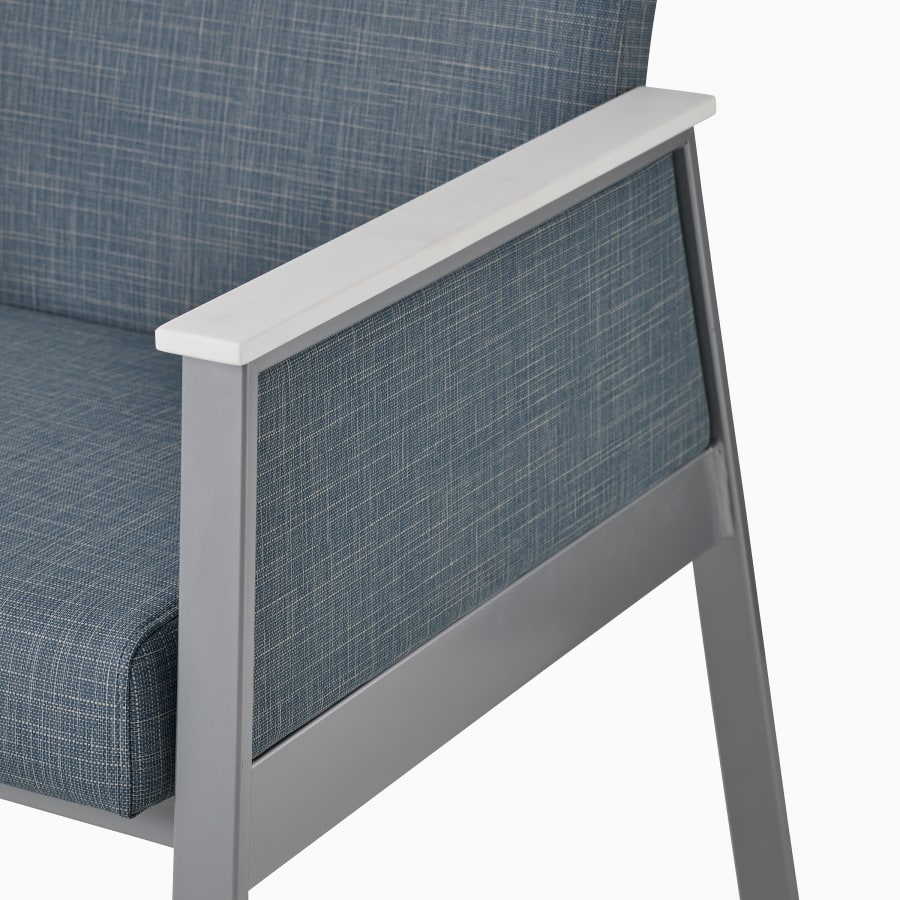 Detail of the arm cap in glacier white Corian for an Easton chair with a closed arm, silver frame, and blue upholstery.