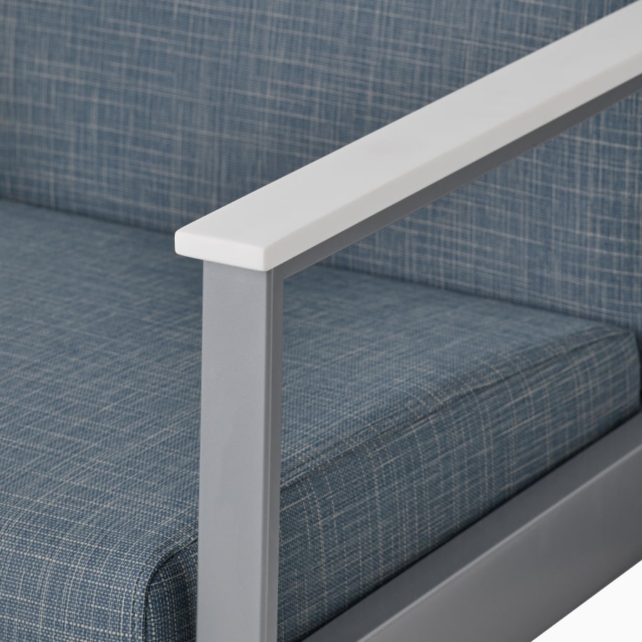Detail of the arm cap in glacier white Corian for an Easton chair with a silver frame and blue upholstery.