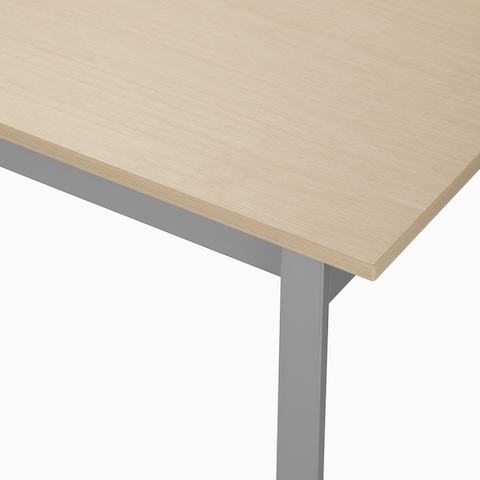 Detail of the top of an Easton table with a clear on ash laminate top and metallic silver leg.