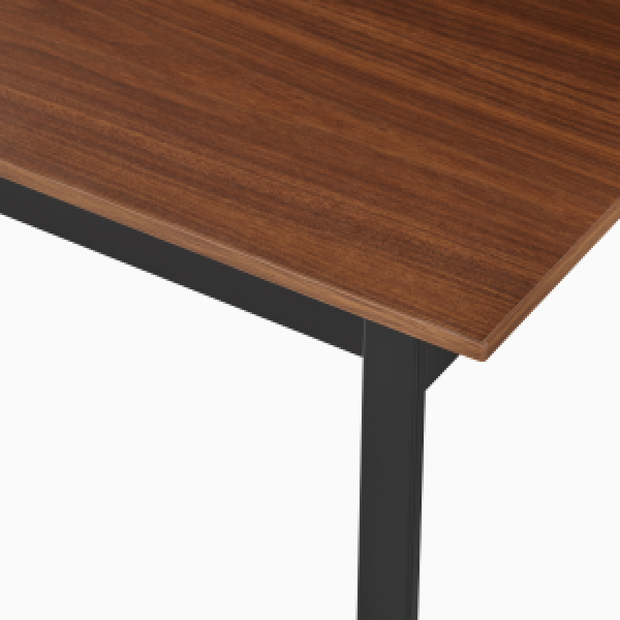 Detail of the top of an Easton table with a medium matte walnut laminate top and black leg.
