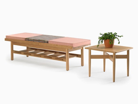 A square Hemlock side table with a potted plant on it and a Tamarack Table and Bench in maple topped with a pink cushion.