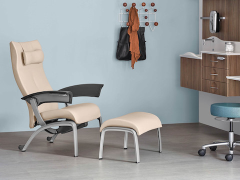 An exam room with a Nemschoff Nala Patient Chair and Ottoman with a physician's stool, with Compass System and an Eames Hang-It-All on the wall.